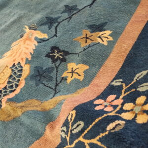 Teal blue rug detail featuring a peach and tan bird motif, dark leaves, and a textured brown border stripe.