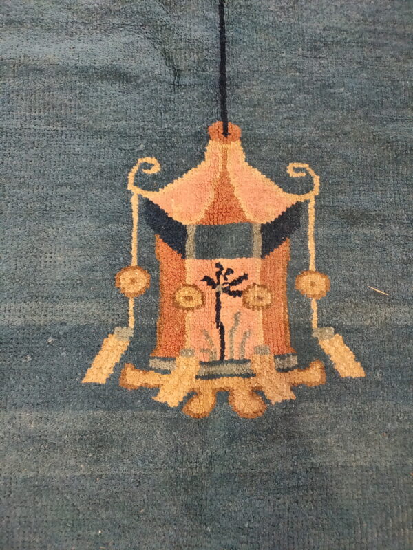 Muted teal rug with a stylized hanging lantern design in salmon, gold, and dark blue.