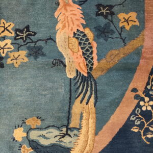 Close-up of a teal rug featuring a stylized peach and gold bird with dark blue leaves.