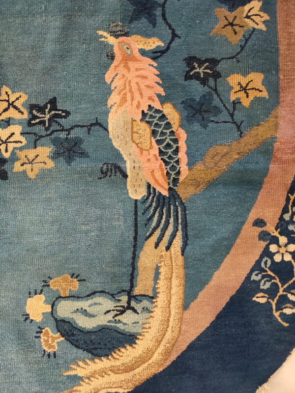Close-up of a teal rug featuring a stylized peach and gold bird with dark blue leaves.