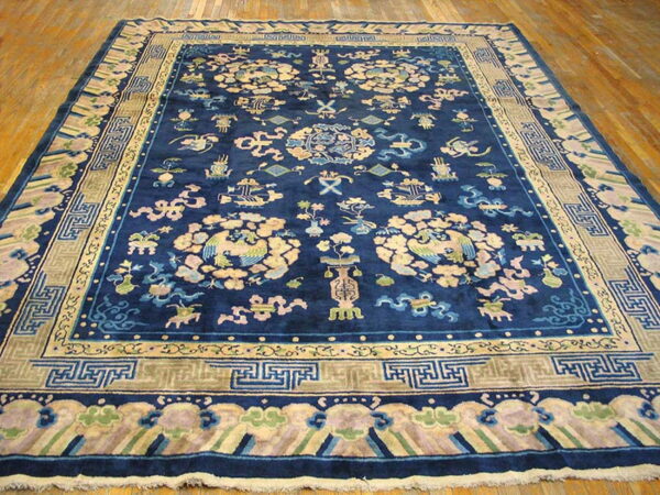 Large navy rug with beige and pale multi-colored traditional motifs and key pattern borders on wood flooring.