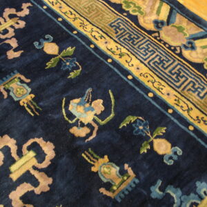 Plush navy blue rug featuring intricate yellow, green, and tan classical motifs rests on a hardwood floor.
