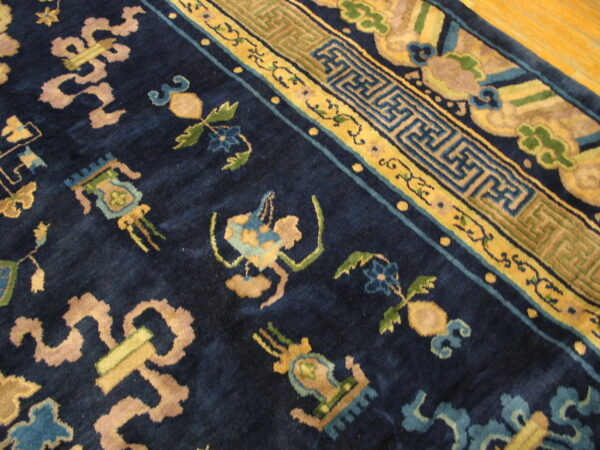 Plush navy blue rug featuring intricate yellow, green, and tan classical motifs rests on a hardwood floor.