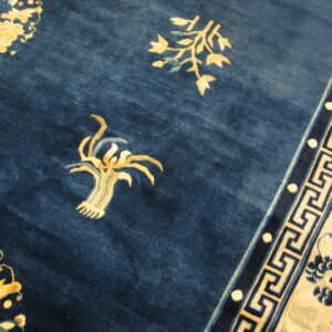 Navy blue rug detail showing gold botanical elements and a cream and blue geometric key border.