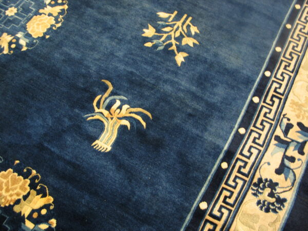 Navy blue rug detail showing gold botanical elements and a cream and blue geometric key border.