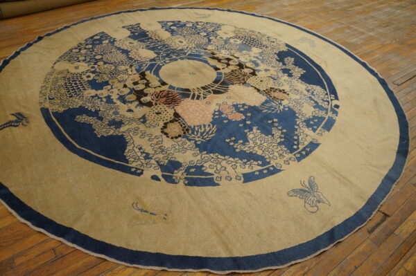 Circular beige rug featuring a detailed blue floral medallion and light pink accents on wood planks.