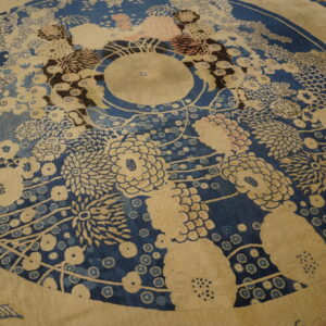 Radial floral rug in deep blue and beige with accents of pink and brown sits on a hardwood floor.