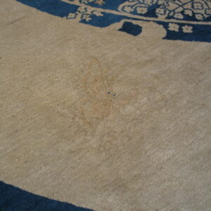 Close-up of a beige rug field with a faint reddish mark and a curved border of dark blue patterns.