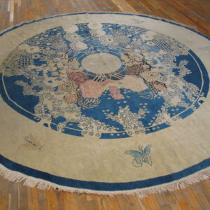 Circular blue and tan rug with a floral medallion pattern and fringed border on wood planks.