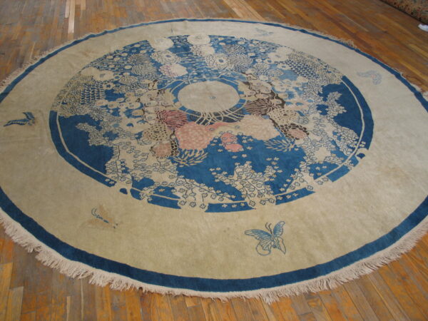 Circular blue and tan rug with a floral medallion pattern and fringed border on wood planks.