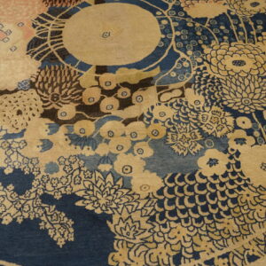 Detailed view of a low-pile rug showing large stylized flowers in tan and soft pink against dark blue.