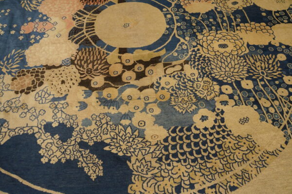 Detailed view of a low-pile rug showing large stylized flowers in tan and soft pink against dark blue.
