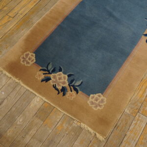 Low-pile dusty blue rug with a tan floral border is laid upon aged wooden plank flooring.