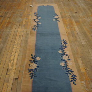 Low-pile blue and tan runner rug with a floral pattern rests on rustic oak wood flooring.