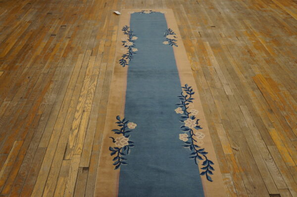 Low-pile blue and tan runner rug with a floral pattern rests on rustic oak wood flooring.