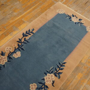 Blue rug with tan border and pink floral vines lays on distressed, yellow-toned wood floors.