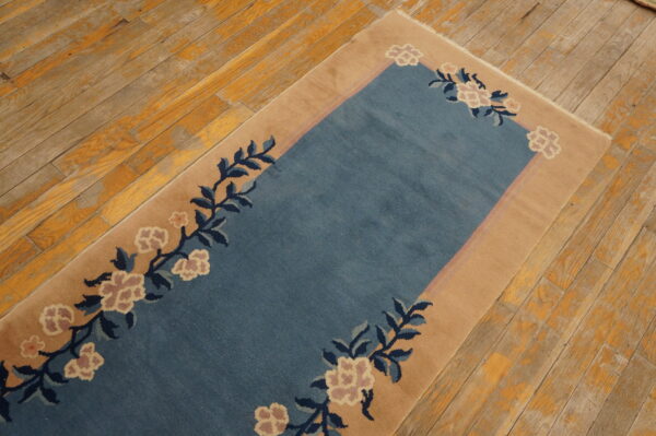 Blue rug with tan border and pink floral vines lays on distressed, yellow-toned wood floors.