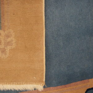 Detailed view of the woven tan rug backing, white fringe, and adjacent plush blue pile.