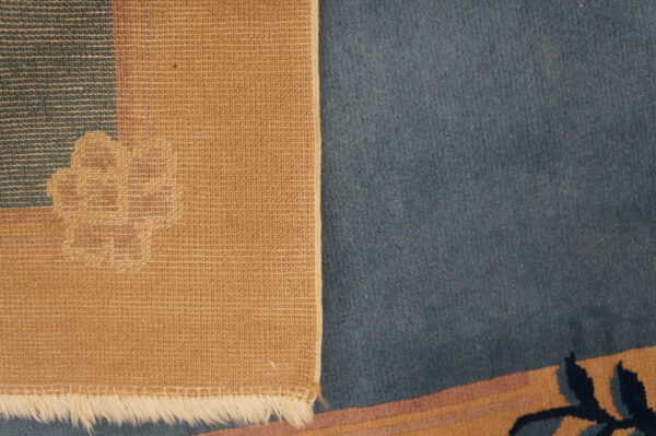 Detailed view of the woven tan rug backing, white fringe, and adjacent plush blue pile.