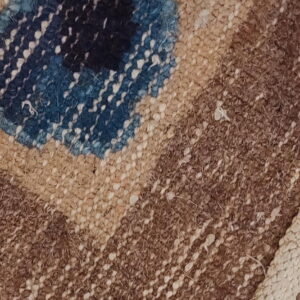 Detail of a textured brown rug with a geometric pattern, blue accent shape, and thick woven edge.