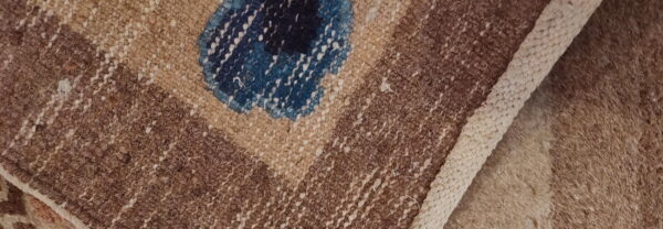 Detail of a textured brown rug with a geometric pattern, blue accent shape, and thick woven edge.