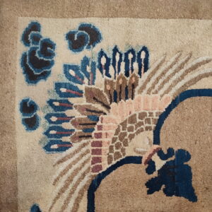 Intricate beige rug detail with dark blue, pink, and brown stylized feathered or floral designs on tile flooring.