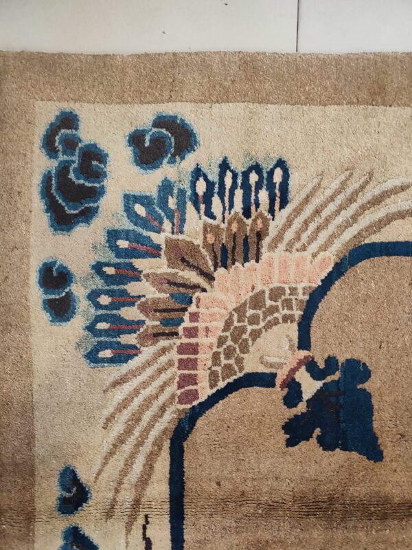 Intricate beige rug detail with dark blue, pink, and brown stylized feathered or floral designs on tile flooring.
