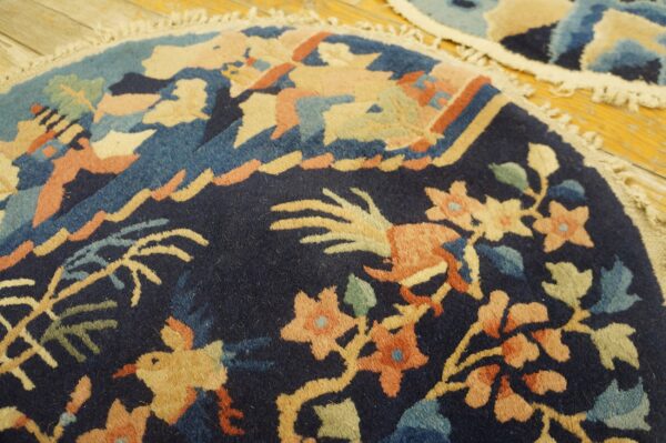 Dark blue, round rug with intricate peach, tan, and teal floral and bird motifs on distressed wood.