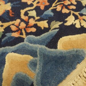 High-pile navy rug with tan and coral floral pattern, showing its carved texture, fringe, and wood floor.