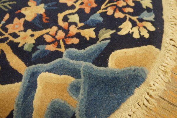 High-pile navy rug with tan and coral floral pattern, showing its carved texture, fringe, and wood floor.