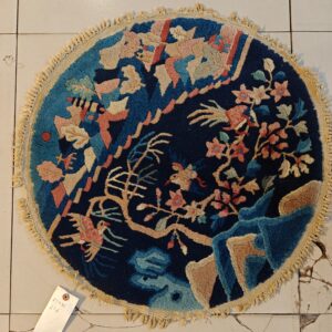 A circular navy rug with a high-pile floral and bird pattern in pinks, tan, and blues rests on cracked white tile.