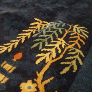 Close-up of a high-pile dark blue rug featuring a gold, green, and orange botanical pattern.