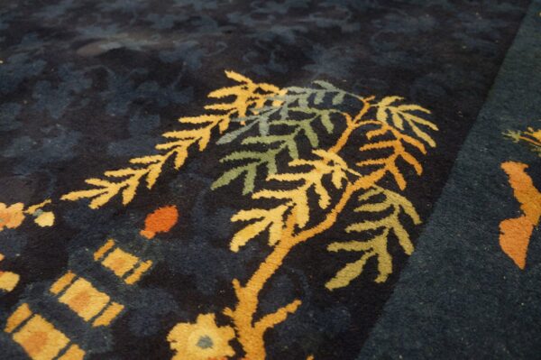 Close-up of a high-pile dark blue rug featuring a gold, green, and orange botanical pattern.