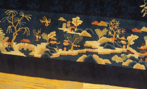 Navy blue rug border shows a detailed gold, rust, and green landscape pattern over wood flooring.