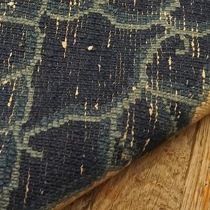 Detail showing a dark blue patterned rug edge and tan border resting on weathered wooden planks.