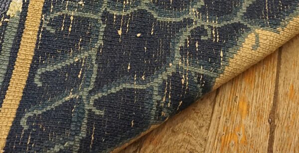 Detail showing a dark blue patterned rug edge and tan border resting on weathered wooden planks.