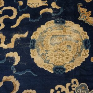 Detail of a deep blue rug showing a tan mythical beast medallion and stylized floral patterns.