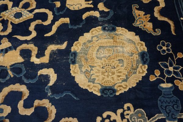 Detail of a deep blue rug showing a tan mythical beast medallion and stylized floral patterns.