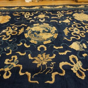 Deep indigo rug featuring intricate gold and light blue ornamental designs is shown on a wooden floor.