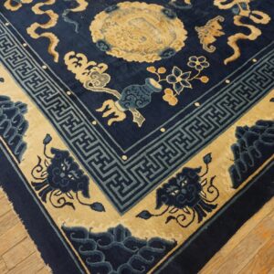 Navy rug with beige motifs and blue geometric fretwork borders rests on light-colored wood planks.