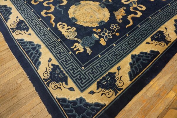 Navy rug with beige motifs and blue geometric fretwork borders rests on light-colored wood planks.