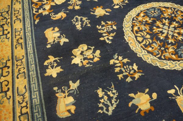 Navy blue rug with scattered gold and rust floral motifs, a partial medallion, and geometric banded borders.