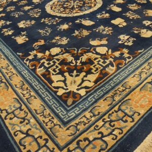 Navy blue rug with a patterned gold and blue border and floral motifs rests on worn wood flooring.