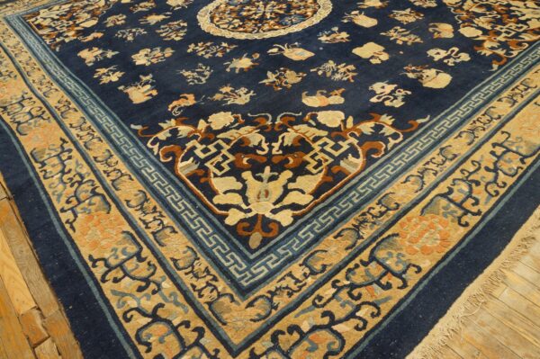 Navy blue rug with a patterned gold and blue border and floral motifs rests on worn wood flooring.