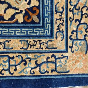 Close-up of a high-pile blue and beige rug corner with complex scrolling and Greek key borders.