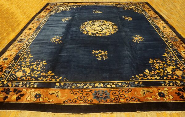 A deep blue rug with a gold central medallion and ornate rust-colored borders on wood planks.