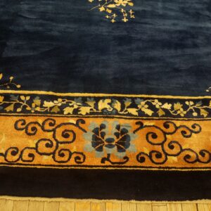Close-up of a high-pile navy rug with a wide gold and blue stylized floral border resting on wood flooring.