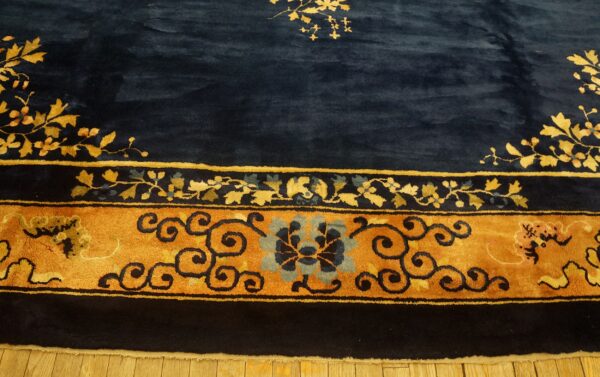 Close-up of a high-pile navy rug with a wide gold and blue stylized floral border resting on wood flooring.