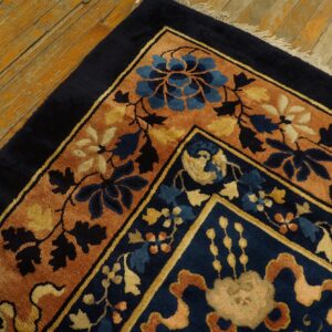 A navy blue rug with rust, blue, and yellow floral borders rests on worn plank flooring.