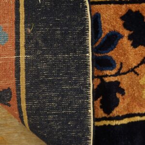The edge of a floral brown and navy high-pile rug is folded over, revealing the woven back on wood.